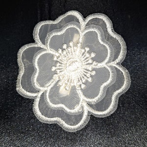 May include: A white lace flower with a delicate design. The flower has multiple layers of lace and a small, intricate center.