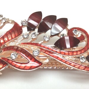 May include: A red and gold peacock hair clip with clear and red rhinestones. The clip is designed with a peacock feather pattern and has a decorative swirl design.