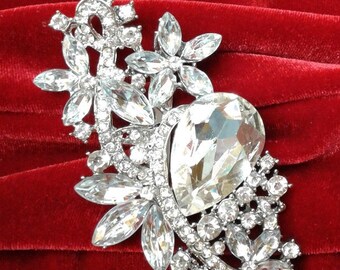 May include: A silver brooch with a large clear crystal in the center, surrounded by smaller crystals in a floral design.