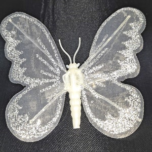May include: A white butterfly with silver glitter accents. The butterfly is made of a sheer fabric and has a delicate, feminine look.