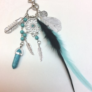 May include: A silver-toned keychain with a dreamcatcher design, turquoise beads, and feather accents. The keychain features a turquoise crystal pendant and black and teal feathers. The design is intricate and detailed.