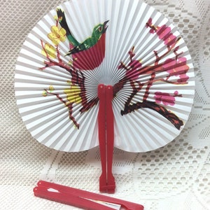 May include: A white folding fan with a red, green, and yellow bird on a branch with pink flowers. The fan has a red handle.