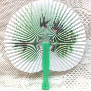 May include: A white paper folding fan with a green handle. The fan features a design of swallows flying over green reeds.