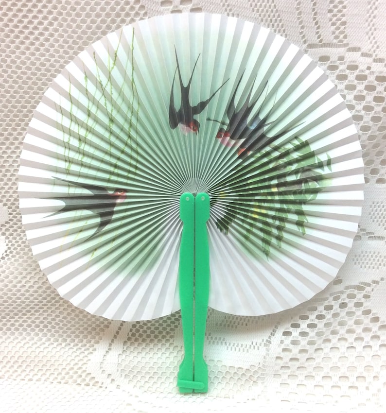 May include: A white paper folding fan with a green handle. The fan features a design of swallows flying over green reeds.