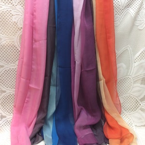 May include: Seven sheer scarves in a rainbow of colors, including pink, blue, purple, orange, and yellow. The scarves are arranged in a row, with the pink scarf on the left and the yellow scarf on the right.