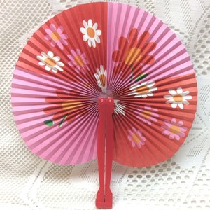 May include: A red and pink paper folding fan with a floral design. The fan has a red plastic handle.