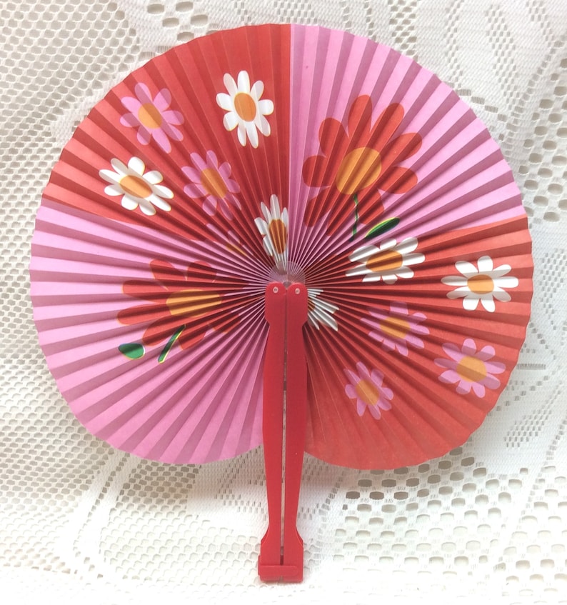 May include: A red and pink paper folding fan with a floral design. The fan has a red plastic handle.