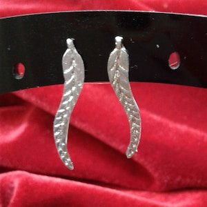 May include: A pair of silver earrings with a leaf design. The earrings are hanging from a black display stand.