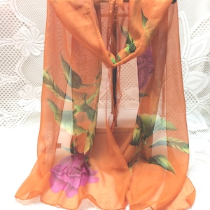 May include: A sheer orange scarf with a floral print featuring pink roses and green leaves.