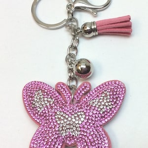 May include: Pink butterfly keychain with rhinestones and a silver chain. The keychain has a silver ring and a pink tassel.