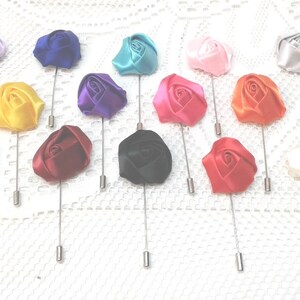 May include: Assortment of 18 silk rose lapel pins in various colors, including white, pink, red, orange, yellow, green, blue, purple, and black. Each pin features a single rose with a silver pin.