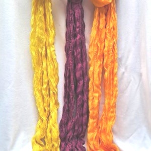 May include: Three long, thin scarves in yellow, purple, and orange. The scarves are made of a soft, crinkled fabric and are hanging on a white hanger.