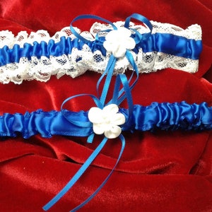 May include: Two blue and white garters with white satin flowers. The garters are made of lace and satin.