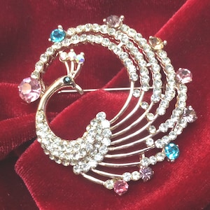May include: A gold-tone peacock brooch with clear and colorful rhinestones. The peacock's tail feathers are made of rows of clear rhinestones.