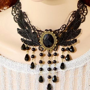 May include: Black lace choker necklace with a large black gemstone pendant and dangling black beads. The pendant is surrounded by a gold-toned metal frame.