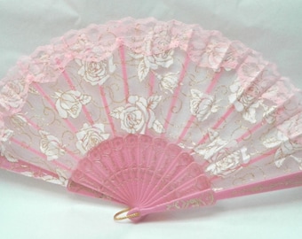 May include: A pink hand fan with a white lace overlay and a floral design. The fan is closed and has a pink handle.