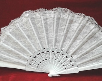 May include: A white lace hand fan with a white plastic frame. The fan is closed and has a scalloped edge.