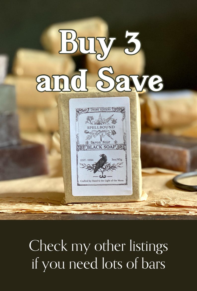 Op de afbeelding: Een stuk zwarte zeep verpakt in bruin papier met een etiket met de tekst "Spellbound Black Soap". Het etiket toont een illustratie van een raaf en de tekst "Buy 3 and Save". De zeep weegt 85g.