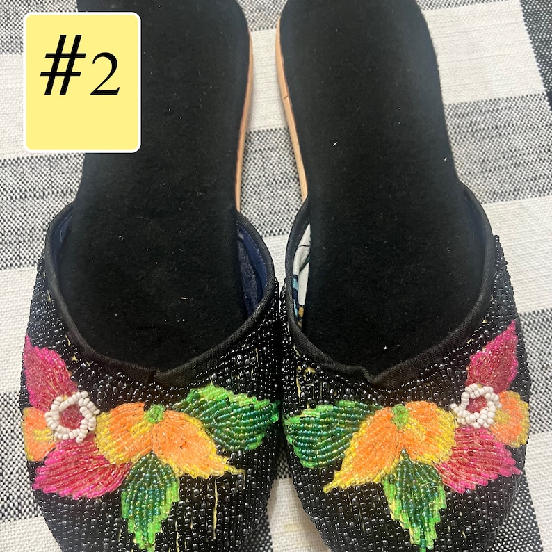 以下が含まれることがあります： カラフルな花の刺繍が施された、黒いビーズのスリッポンシューズのペア。花はピンク、オレンジ、緑のビーズが特徴です。靴の内側は黒で、明るい色のソールが付いています。「#2」の数字が左上の黄色のボックスにあります。
