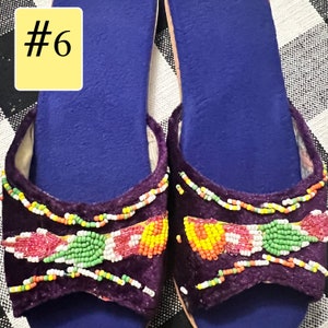 以下が含まれることがあります： 紫色のベルベットのスリッポンサンダル一足。ビーズの装飾が施されています。サンダルは青いフットベッドで、赤、緑、黄色、白の模様のカラフルなビーズで飾られています。「#6」の数字が左上の黄色の長方形にあります。