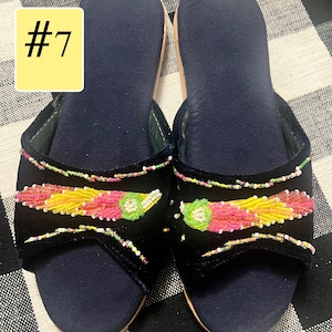 以下が含まれることがあります： カラフルなビーズ装飾が施された、ネイビーブルーのベルベットスリッパのペア。スリッパはピンク、黄色、緑色のビーズのデザインが特徴です。「#7」の数字が左上の黄色の長方形に表示されています。
