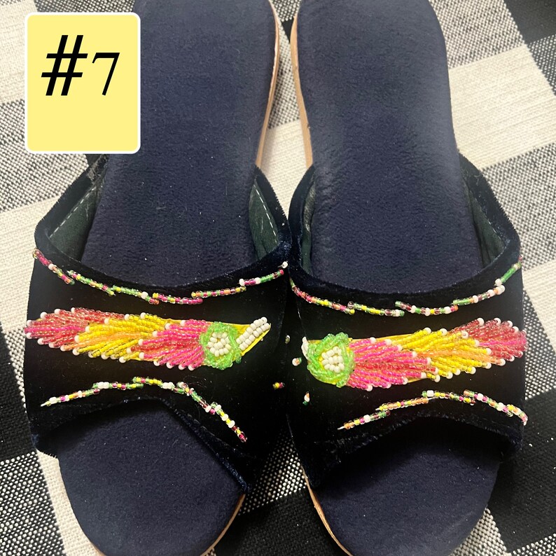 以下が含まれることがあります： カラフルなビーズ装飾が施された、ネイビーブルーのベルベットスリッパのペア。スリッパはピンク、黄色、緑色のビーズのデザインが特徴です。「#7」の数字が左上の黄色の長方形に表示されています。