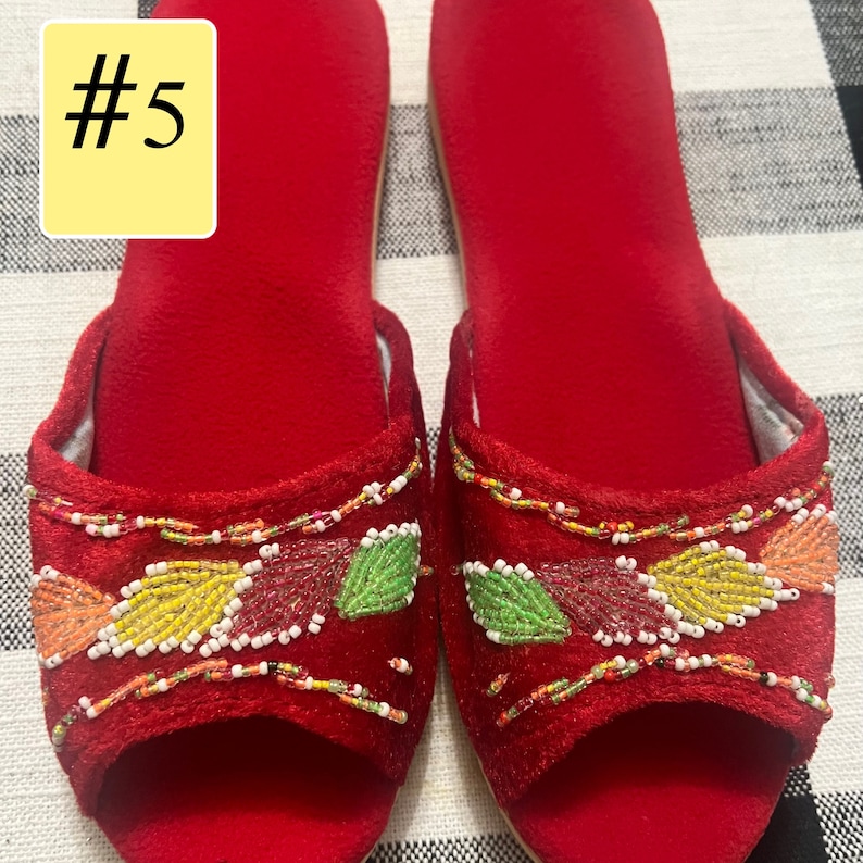 以下が含まれることがあります： 赤いベルベットのオープントゥスリッパのペア。スリッパは、オレンジ、イエロー、グリーン、レッドの色合いのビーズの葉のデザインで装飾されています。「#5」の数字が左上の黄色の長方形にあります。
