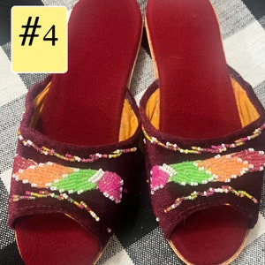 以下が含まれることがあります： ピンク、オレンジ、緑色のビーズの花柄が施された、バーガンディ色のベルベットオープントゥサンダル。サンダルは柔らかい赤色の内側と明るい色のソールです。「#4」の数字が左上の黄色のボックスにあります。