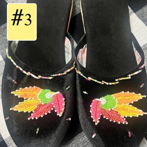 以下が含まれることがあります： ピンク、黄色、緑の色合いのビーズの花柄が施された黒いベルベットのスリッパのペア。縁はカラフルなビーズでトリミングされています。スリッパは柔らかい柄の裏地で、「#3」の数字が黄色のボックスに入っています。