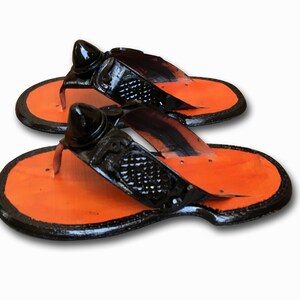 May include: A pair of black leather sandals with orange soles and a pointed toe. The sandals have a decorative design on the strap.