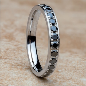 Könnte beinhalten: Ein silberner Bandring mit einer Reihe schwarzer Diamanten, die um die gesamte Band gefasst sind.
