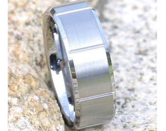 May include: A silver tungsten carbide ring with a beveled edge and a brushed finish. The ring has a grooved design on the top.