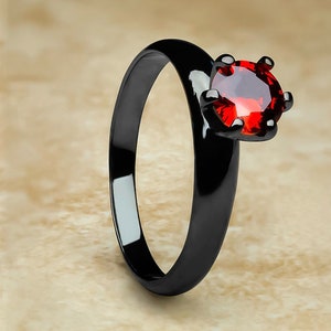 May include: A black ring with a red gemstone. The ring is made of stainless steel and has a polished finish.