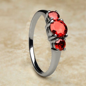 May include: A silver ring with three red gemstones. The ring has a simple band and the gemstones are set in a prong setting.