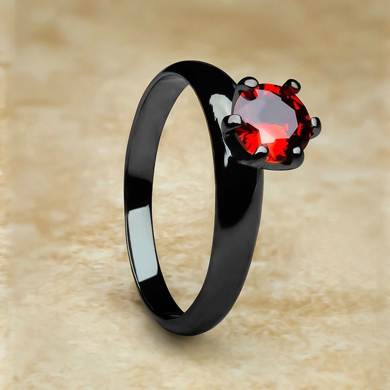 May include: A black ring with a red gemstone. The ring is made of stainless steel and has a polished finish.