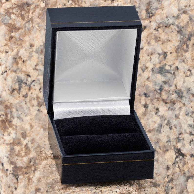 K&ouml;nnte beinhalten: Eine schwarze Ringbox mit wei&szlig;er Satin-Auskleidung und schwarzem Samt-Innenraum. Die Box ist ge&ouml;ffnet und leer.