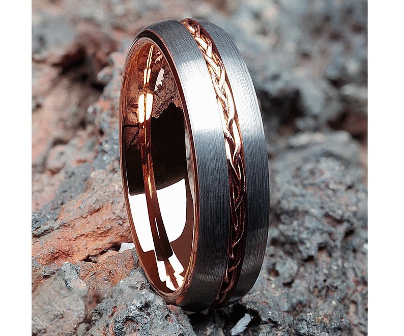 May include: A silver tungsten carbide ring with a rose gold inlay featuring a braided design.