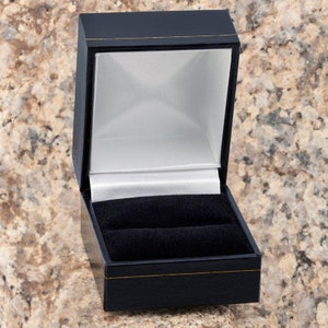 May include: A black ring box with a white satin lining and a black velvet interior. The box is open and empty.
