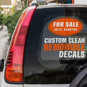 May include: A white car with a rear window sticker that says "FOR SALE (012) 3456789 CUSTOM CLEAR REMOVABLE DECALS".