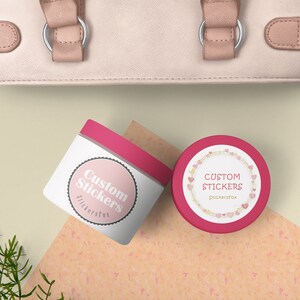 May include: Two pink and white round containers with lids. The containers have a white label with the text "Custom Stickers" in pink lettering. One container has a pink heart border around the label.