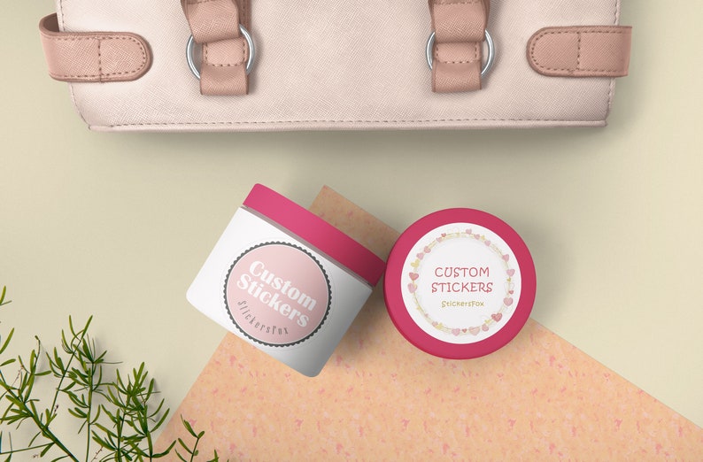 May include: Two pink and white round containers with lids. The containers have a white label with the text "Custom Stickers" in pink lettering. One container has a pink heart border around the label.