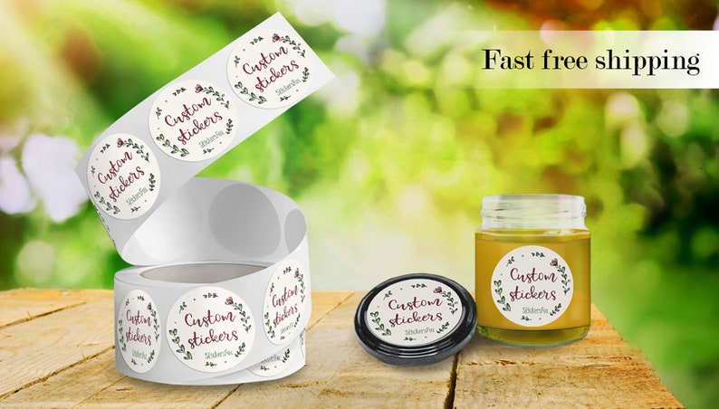 May include: Roll of round, white stickers with a floral design and the text "Custom Stickers" in burgundy lettering. A jar of honey with a similar sticker is shown in the background.