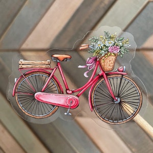 May include: A red bicycle with a basket full of flowers. The bicycle has a wooden crate on the back and a wicker basket on the front.