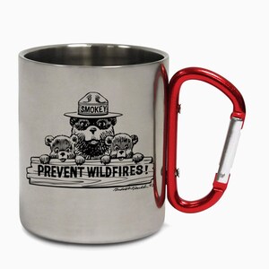 Può includere: Una tazza in acciaio inossidabile con un manico a moschettone rosso. La tazza presenta un'illustrazione in bianco e nero di Smokey Bear e due cuccioli con il testo "Prevent Wildfires!"