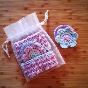 May include: Set of four crocheted flower-shaped makeup remover pads in shades of purple and blue, packaged in a white organza bag.