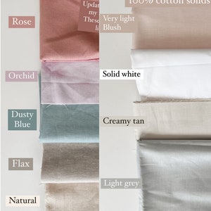 Op de afbeelding: Gevouwen stoffen stalen in verschillende kleuren, waaronder roos, orchidee, stoffig blauw, vlas en naturel. Andere stalen zijn gelabeld als zeer lichtroze, effen wit, cr&egrave;mekleurig bruin en lichtgrijs. De tekst "100% katoenen solids" is ook zichtbaar.