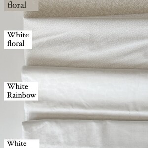 Op de afbeelding: Een stapel 100% katoenen prints in verschillende patronen. De stoffen zijn onder andere "Creamy floral", "White floral", "White Rainbow" en "White Snowflake". De stoffen zijn wit en gebroken wit.