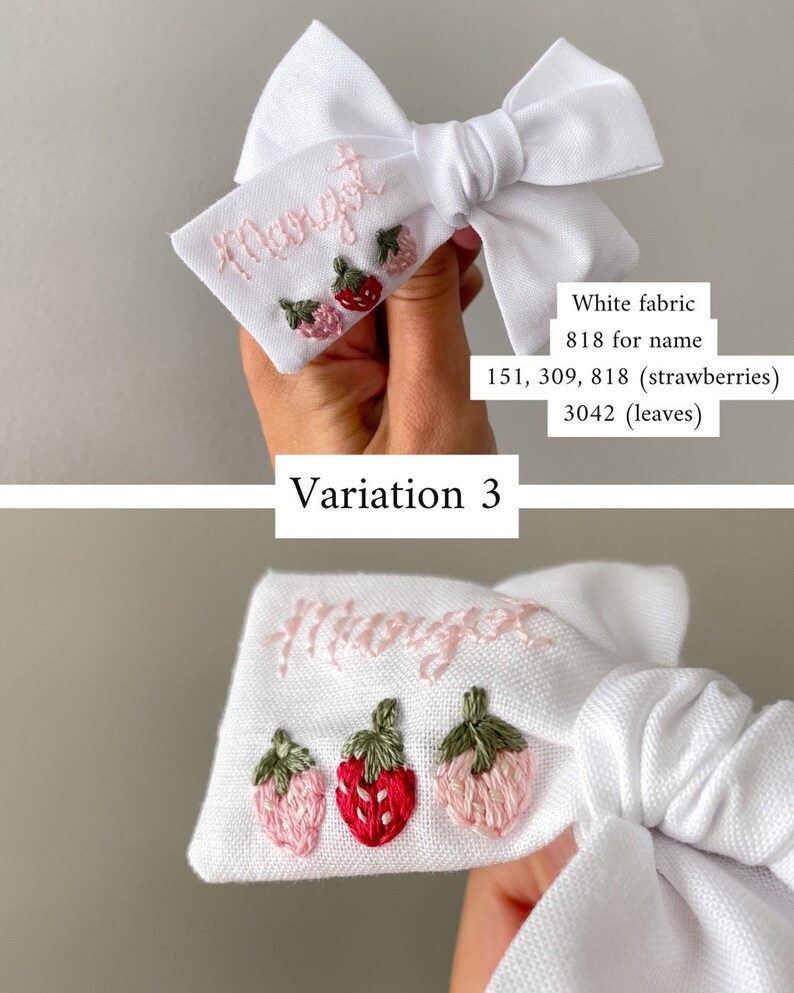 Op de afbeelding: Witte stoffen haarstrik met geborduurde naam en aardbeienontwerp. De naam is lichtroze en de aardbeien zijn in roze en rode tinten met groene bladeren. Variatie 3.