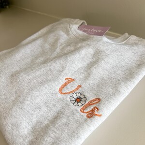May include: A gray sweatshirt with the word "Vols" embroidered in orange with a white daisy in the center of the word.