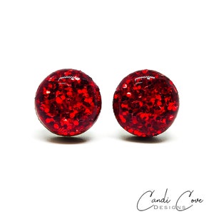 May include: A pair of red glitter stud earrings. The earrings are round and have a shiny, sparkly finish.